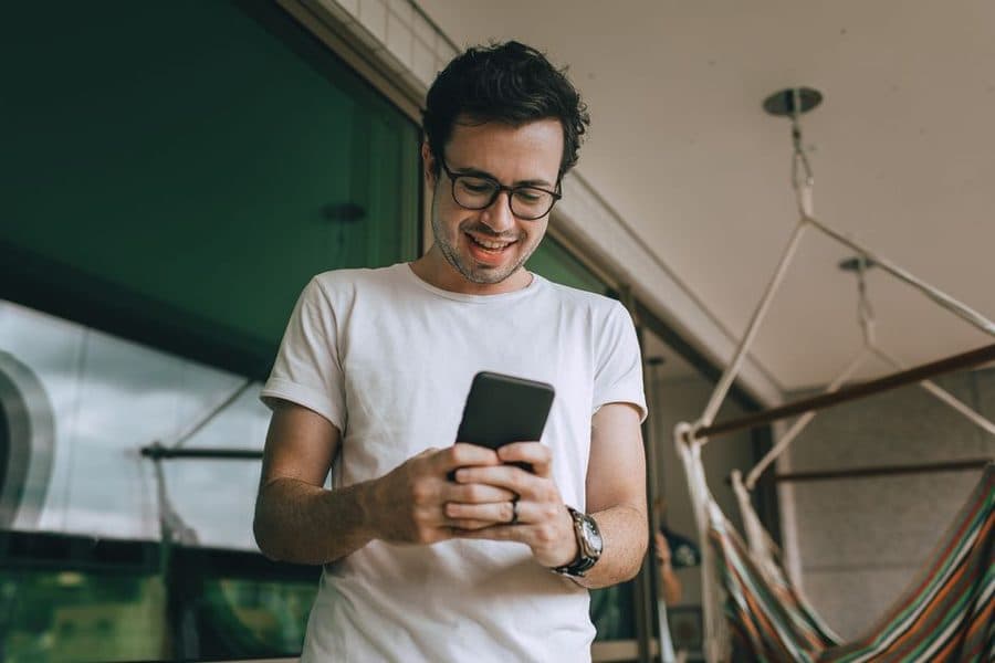 Man smiling at his phone on a home balcony